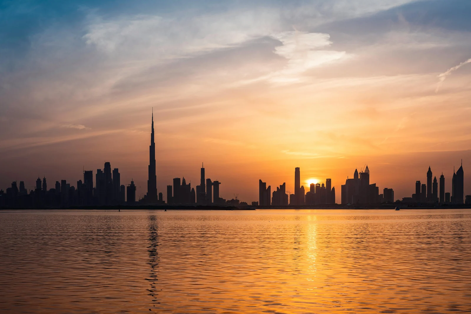 Dubai skyline and the Burj Khalifa across the water at sunset.